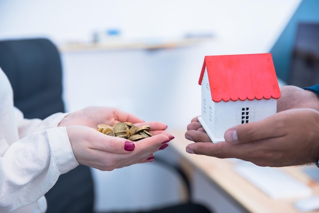 Soldi della mano della donna con il modello della casa della mano dell'uomo