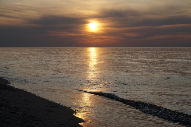 Sole che si riflette nelle onde sulla riva al tramonto