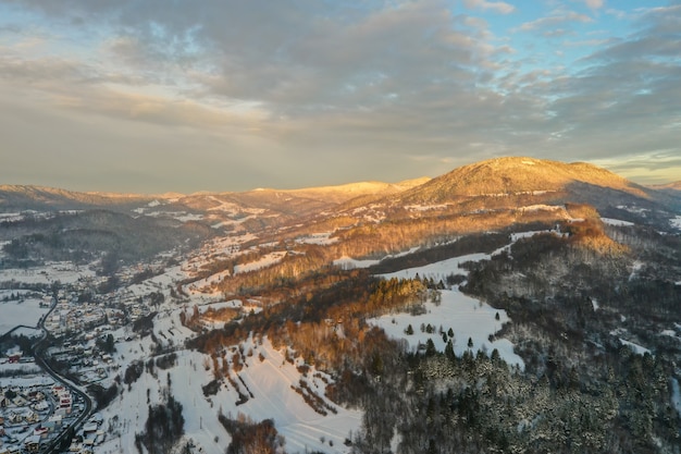 Sole che splende sulle montagne innevate sopra il villaggio e la strada nella sera d'inverno.