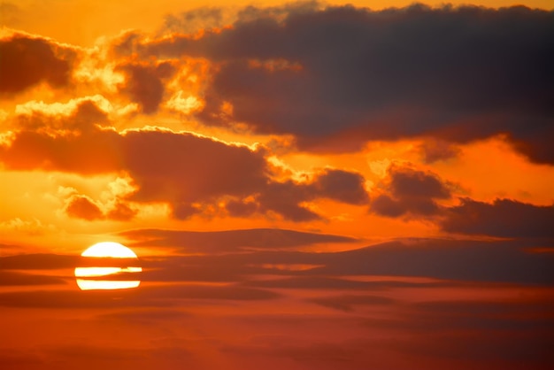 Sole splendente in un cielo arancione con nuvole scure al tramonto