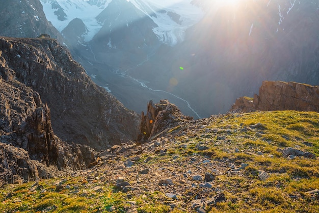 Soleggiata vista sulle montagne dalla scogliera ad altissima quota Paesaggio alpino panoramico con bellissime rocce taglienti e canaloni alla luce del sole Bellissimo scenario sul bordo dell'abisso con pietre taglienti ed erba verde