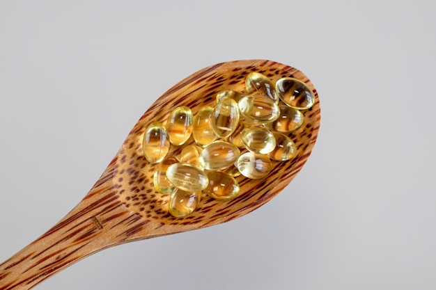 Soleggiate capsule di supplemento di vitamina D3 in un cucchiaio di legno Primo piano Integratori alimentari