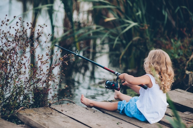 solitario piccolo bambino pesca dal bacino di legno sul lago