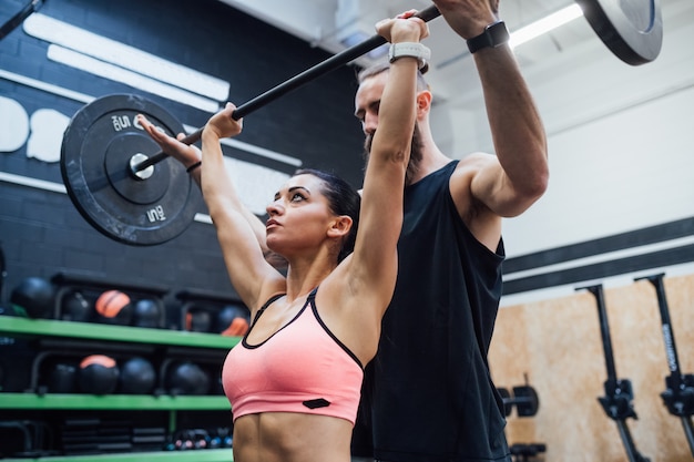 Sollevamento di potenza della giovane donna aiutato dal suo personal trainer