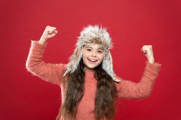 Solo contento. Prendersi cura dei capi in pelliccia. Il cappello morbido dei capelli lunghi del bambino gode della morbidezza. Concetto di moda invernale. Cappello caldo per il freddo. Kid ragazza indossare cappello con paraorecchie sfondo bianco. Accessorio in morbido pelo.