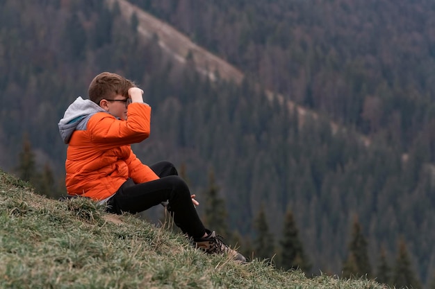 Solo il ragazzo dai capelli castani veglia sulla valle e si siede sul fianco della collina Viaggio escursionistico all'aperto