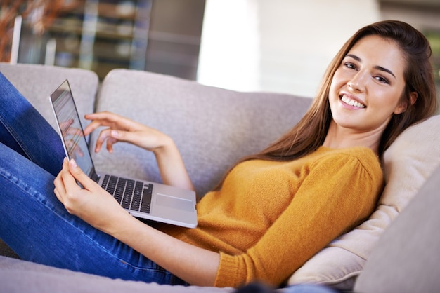 Solo io e il mio laptop Ripresa ritagliata di una giovane donna attraente che si rilassa sul divano con il suo laptop