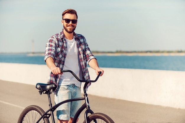 Solo io e la mia bici. Bel giovane in piedi vicino alla sua bicicletta e sorride mentre è all'aperto