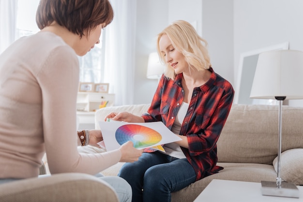 Soluzioni di design. Felici giovani donne positive che si siedono insieme e discutono di una tavolozza di colori mentre scelgono un nuovo design