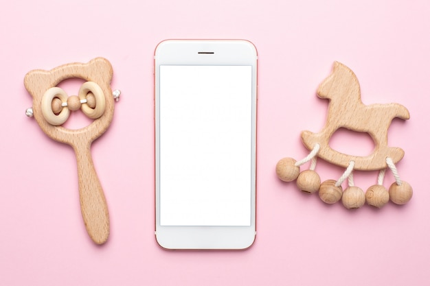 Sonagli e giocattoli di legno del bambino e del telefono cellulare sul rosa