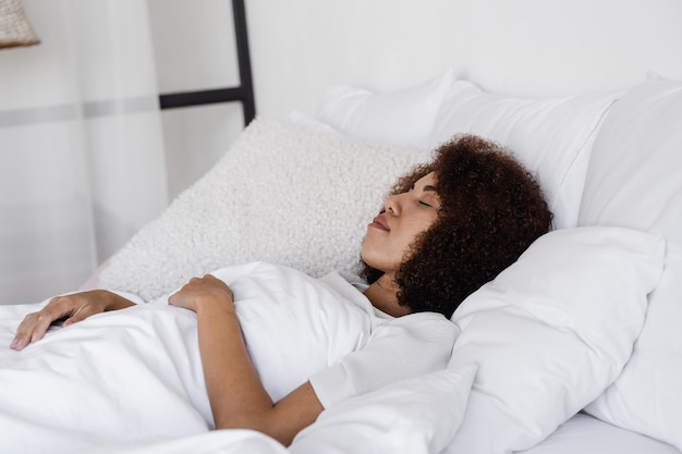 Sonno diurno di una ragazza africana con gli occhi chiusi sdraiato su un letto accogliente a casa Donna afroamericana che si rilassa prima del risveglio