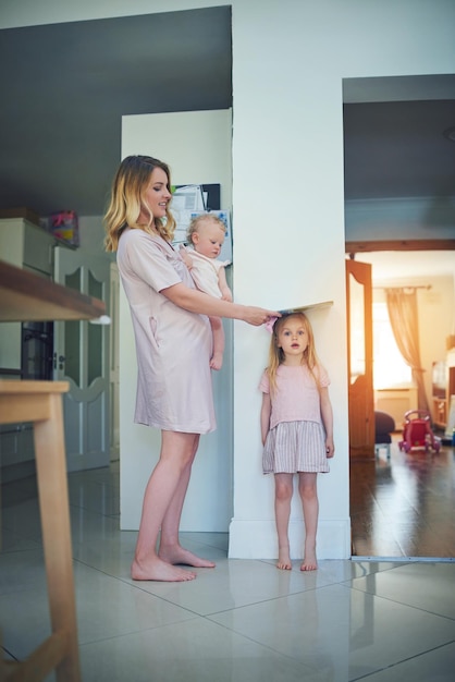 Sono diventato più alto durante la notte Inquadratura di una madre che porta il suo bambino e misura l'altezza delle sue figlie contro un muro