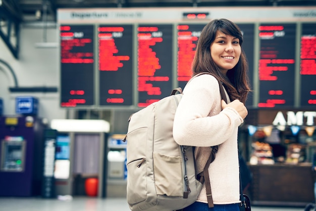 Sono entusiasta di viaggiare Ritratto ritagliato di una giovane donna attraente in piedi a un tabellone degli arrivi e delle partenze dell'aeroporto