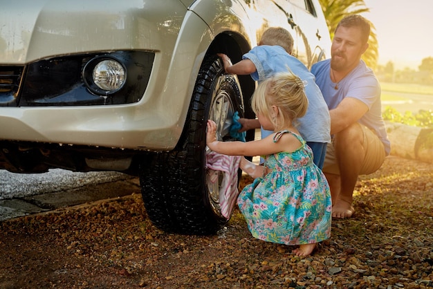 Sono sempre desiderosi di aiutare papà a lavare l'auto. Inquadratura di una famiglia che lava la macchina insieme