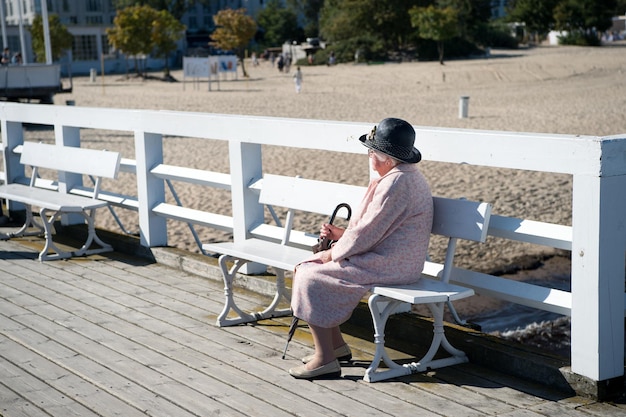 Sopot, Polonia - 19 settembre 2016: elegante donna anziana o vecchia signora si siede su una panca di legno sul molo o sul molo del mare per piacere e passeggiata in giornata di sole sulla spiaggia di sabbia