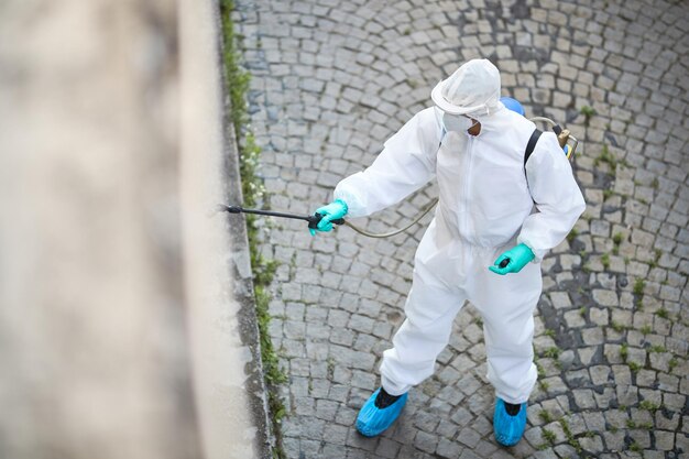 Sopra la vista dell'uomo in tuta ignifuga che disinfetta le strade della città a causa della pandemia di coronavirus