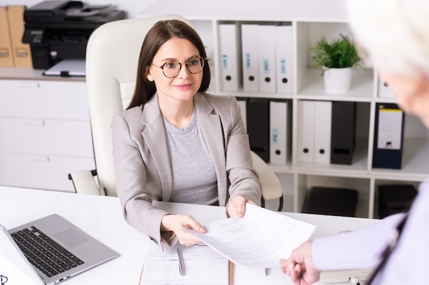 Sopra la vista della spalla della donna maggiore che dà i documenti riempiti al consulente bancario per l'esame