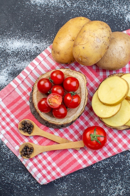 Sopra la vista delle patate crude intere e tritate sui pomodori della tavola di legno sul fondo bianco nero dei colori della miscela