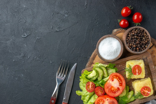 Sopra la vista di formaggio di verdure fresche tritate e intere su tagliere e posate di spezie su superficie nera