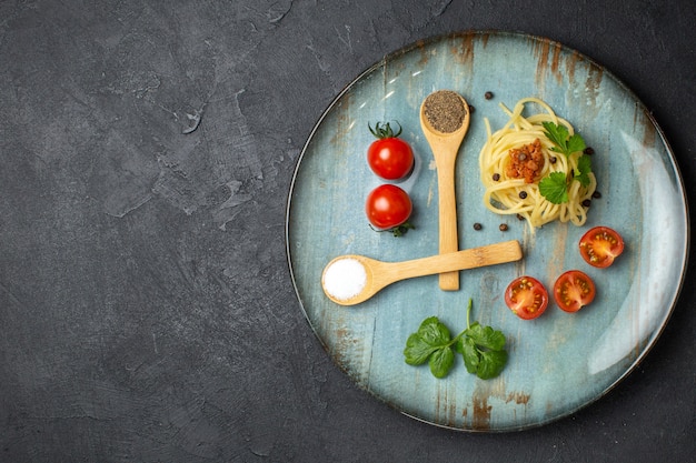 Sopra la vista di una deliziosa pasta servita con pomodori verdi di carne su un piatto sul lato sinistro su sfondo nero