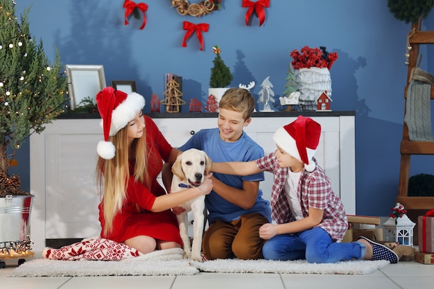 Sorella e fratelli felici che giocano con il cane sul pavimento nella stanza di Natale decorata