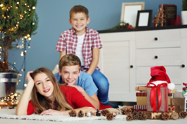 Sorella e fratelli felici con i regali sul pavimento nella stanza di Natale decorata