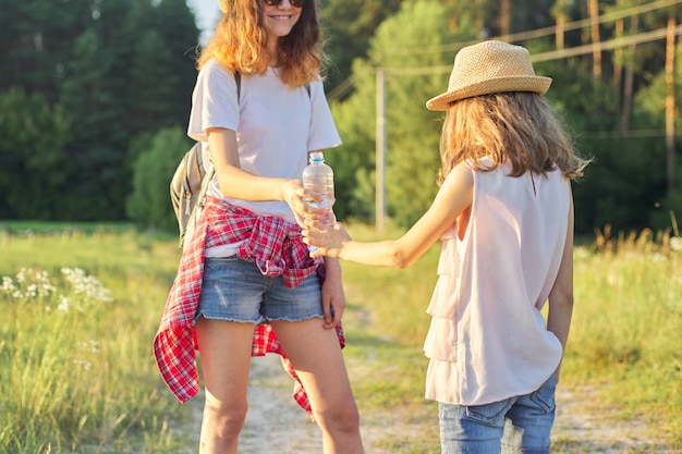 Sorelle delle ragazze dei bambini due con la bottiglia di acqua il giorno di estate caldo in natura