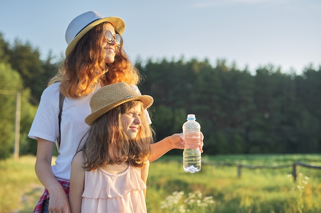 Sorelle delle ragazze dei bambini due con la bottiglia di acqua il giorno di estate caldo in natura