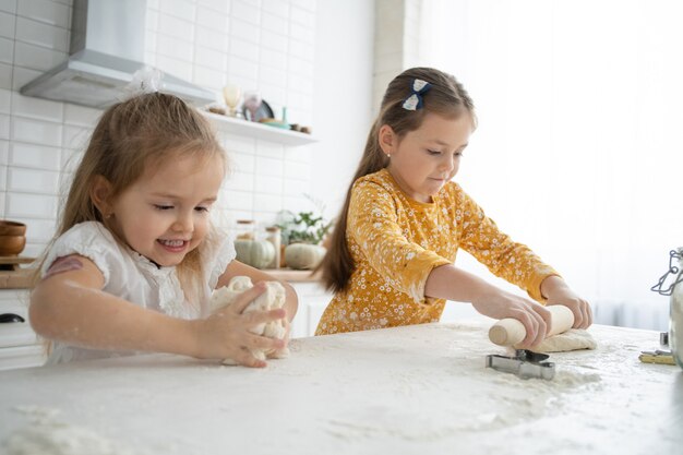 Sorelle felici bambine cuociono biscotti, impastano la pasta, giocano con la farina e ridono in cucina.