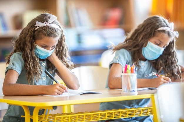 Sorelle gemelle con maschera facciale tornano a scuola durante la quarantena COVID-19.