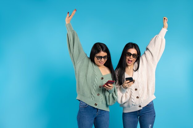 Sorelle gemelle felici in occhiali 3D con smartphone su sfondo blu