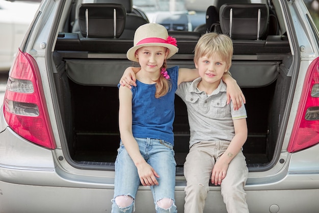 Sorellina e fratello seduti nel bagagliaio di un'auto con le valigie. il concetto di viaggio in famiglia