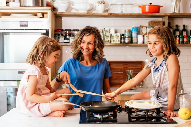 Sorelline che cucinano con sua madre in cucina. Concetto di chef infantile.