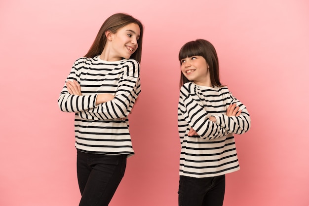 Sorelline ragazze isolate su sfondo rosa guardando sopra la spalla con un sorriso