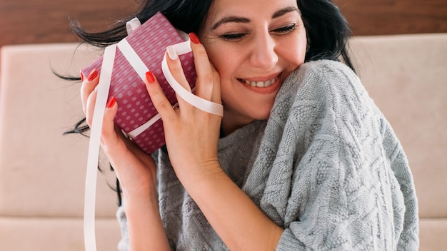 Sorpresa di compleanno romantica Ritratto in primo piano di una donna bruna in un accogliente maglione grigio felice di ricevere un regalo