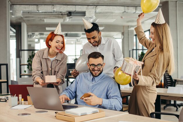 Sorpresa Gente felice di razza mista che festeggia il compleanno di un collega nel moderno officexA