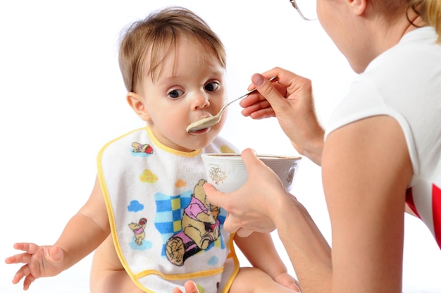 Sorpresa piccola bambina carina mangiare cibo dal cucchiaio Madre che tiene piatto e alimentando il bambino isolato su sfondo bianco
