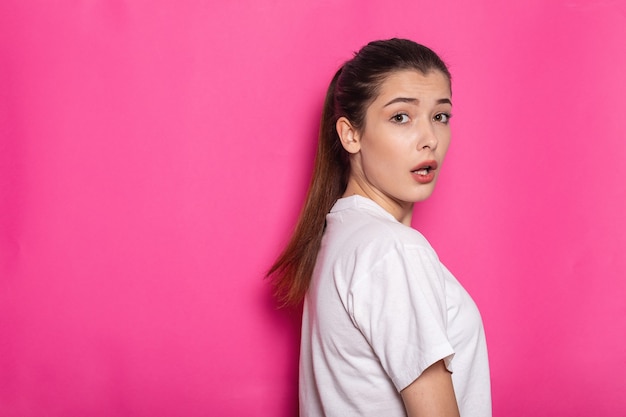 Sorpresa, scioccata giovane donna bruna ragazza in abiti bianchi casual, in posa isolata sul ritratto in studio di sfondo muro rosa pastello. Concetto di stile di vita della gente. Mock up copia spazio. Tenere la bocca aperta