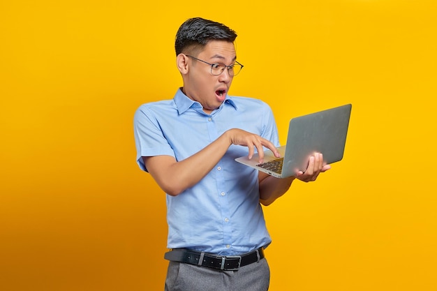 Sorpreso giovane asiatico asiatico in bicchieri utilizzando laptop isolato su sfondo giallo concetto di uomo d'affari e imprenditore