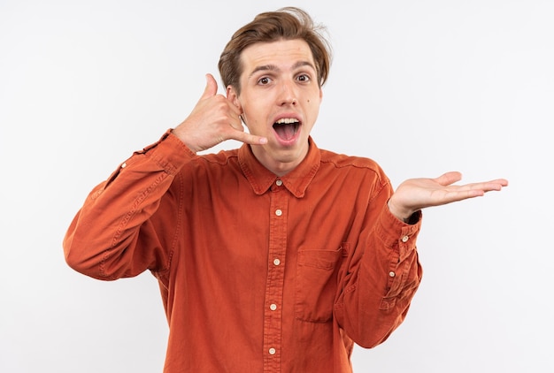 Sorpreso giovane bel ragazzo che indossa una camicia rossa che mostra il gesto di una telefonata che diffonde la mano isolata sul muro bianco