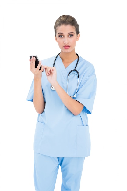 Sorpreso infermiera dai capelli castani in blu scrub utilizzando un telefono cellulare