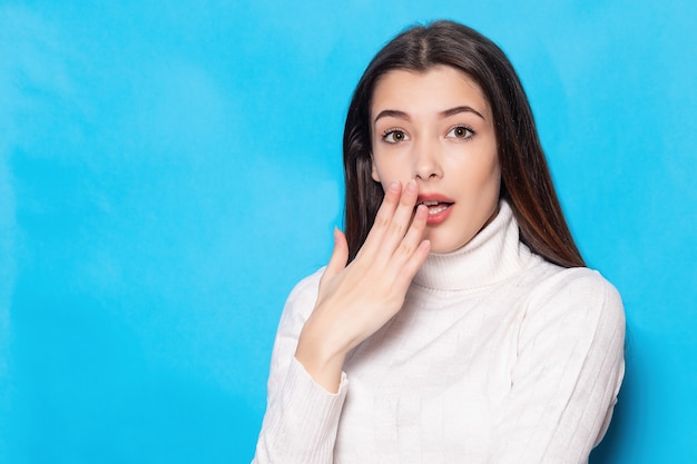 Sorpreso, scioccato giovane donna bruna ragazza in abiti bianchi casual, in posa isolato su sfondo muro blu pastello ritratto in studio. Concetto di stile di vita della gente. Mock up copia spazio. Tenere la bocca aperta