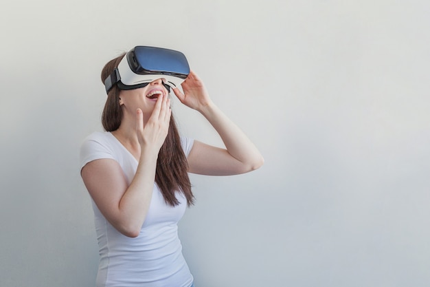 Sorrida la giovane donna che indossa usando la cuffia avricolare del casco di vetro di realtà virtuale VR su bianco