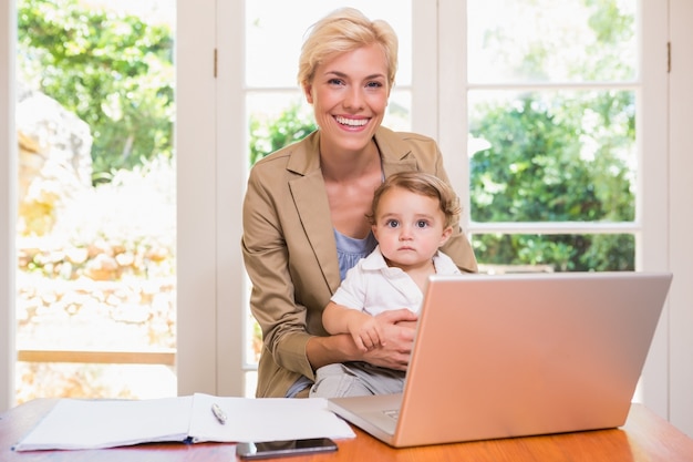 Sorridendo della donna bionda graziosa con suo figlio che per mezzo del computer portatile