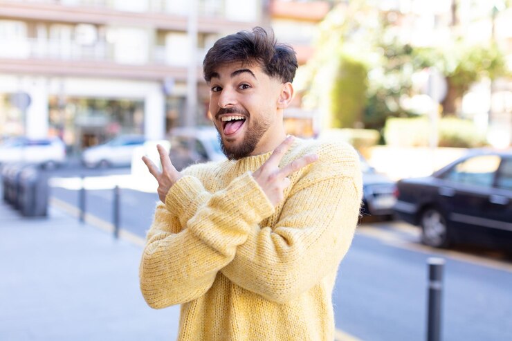 Foto sorridendo e guardando felice, amichevole e soddisfatto, gesticolando vittoria o pace con entrambe le mani
