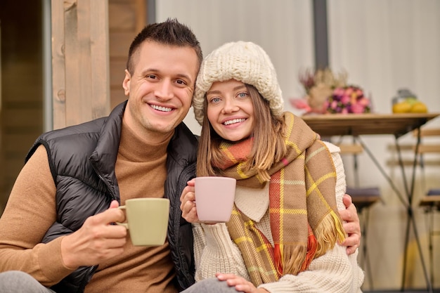 Sorridendo felice bell'uomo romantico e la sua bella compagna compiaciuta che tiene le tazze da caffè