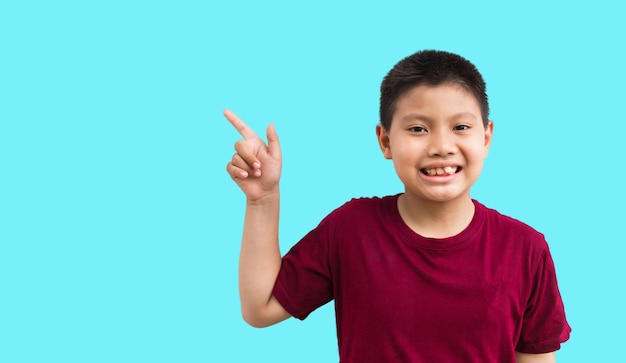 Sorridendo felice ragazzo asiatico che punta il dito lontano nello spazio della copia isolato su uno sfondo blu chiaro