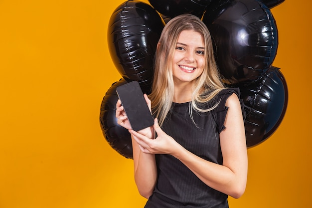 Sorridente affascinante giovane donna con il cellulare con schermo vuoto vuoto su sfondo giallo con mongolfiere ritratto in studio. saldi del venerdì nero