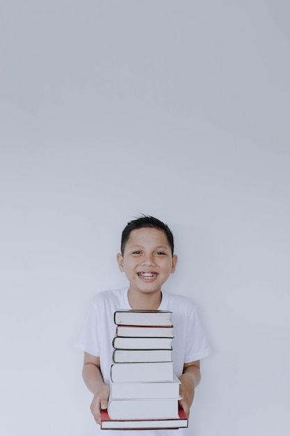 Sorridente allegro ragazzino che tiene pila di libri isolati su sfondo bianco Giornata mondiale del libro