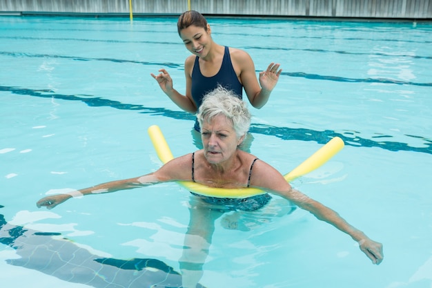 Sorridente allenatore femminile aiutando senior donna in piscina